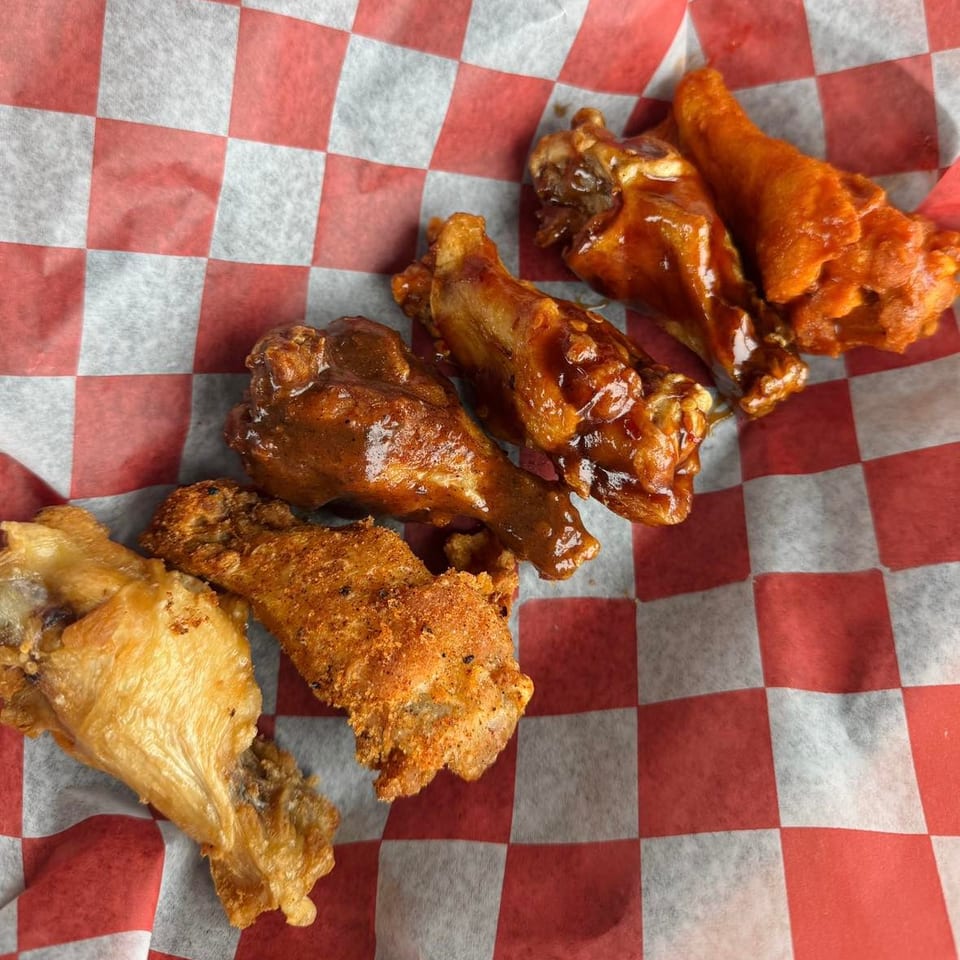 Assortment of chicken wings in various sauces and seasonings on red and white checkered paper.