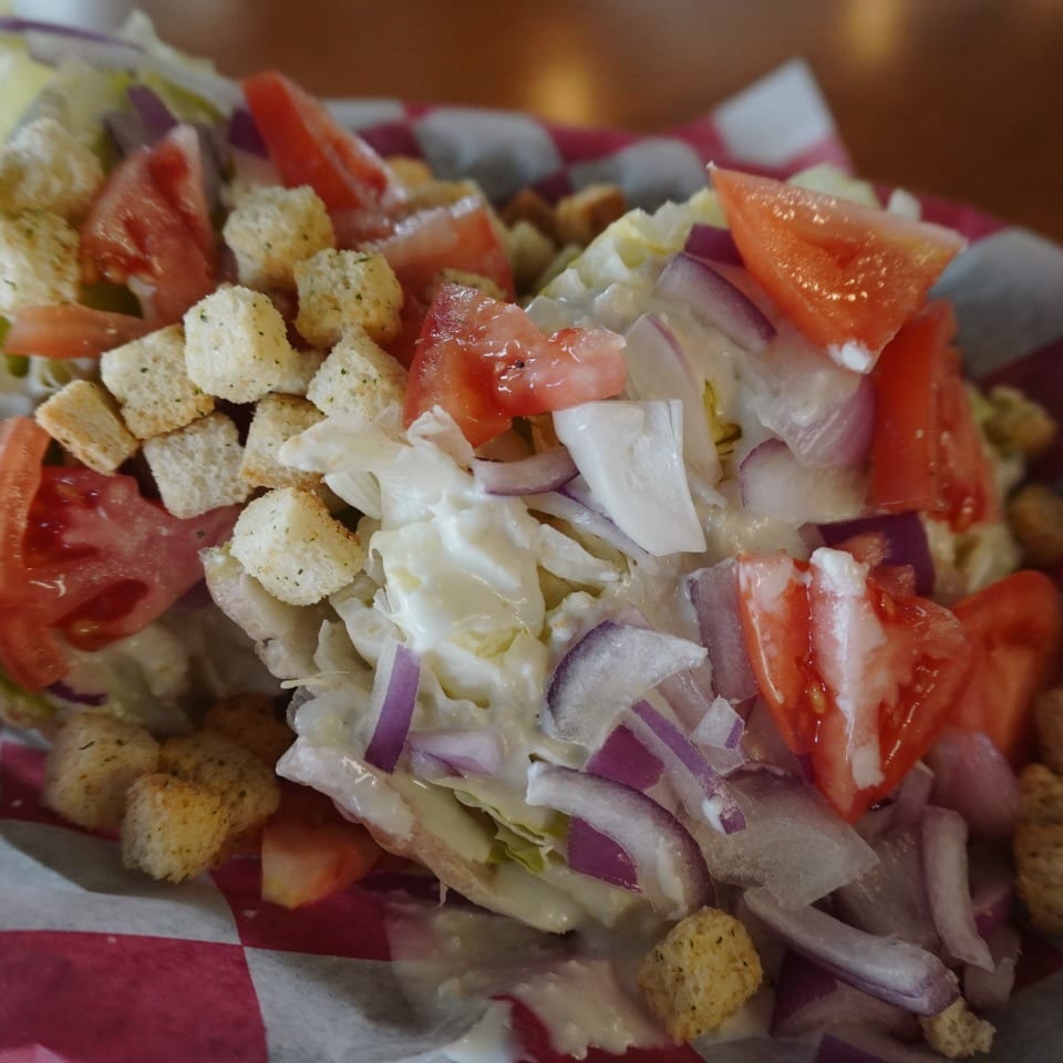 Wedge salad with lettuce, tomatoes, red onions, croutons, and creamy dressing in a red checkered basket.