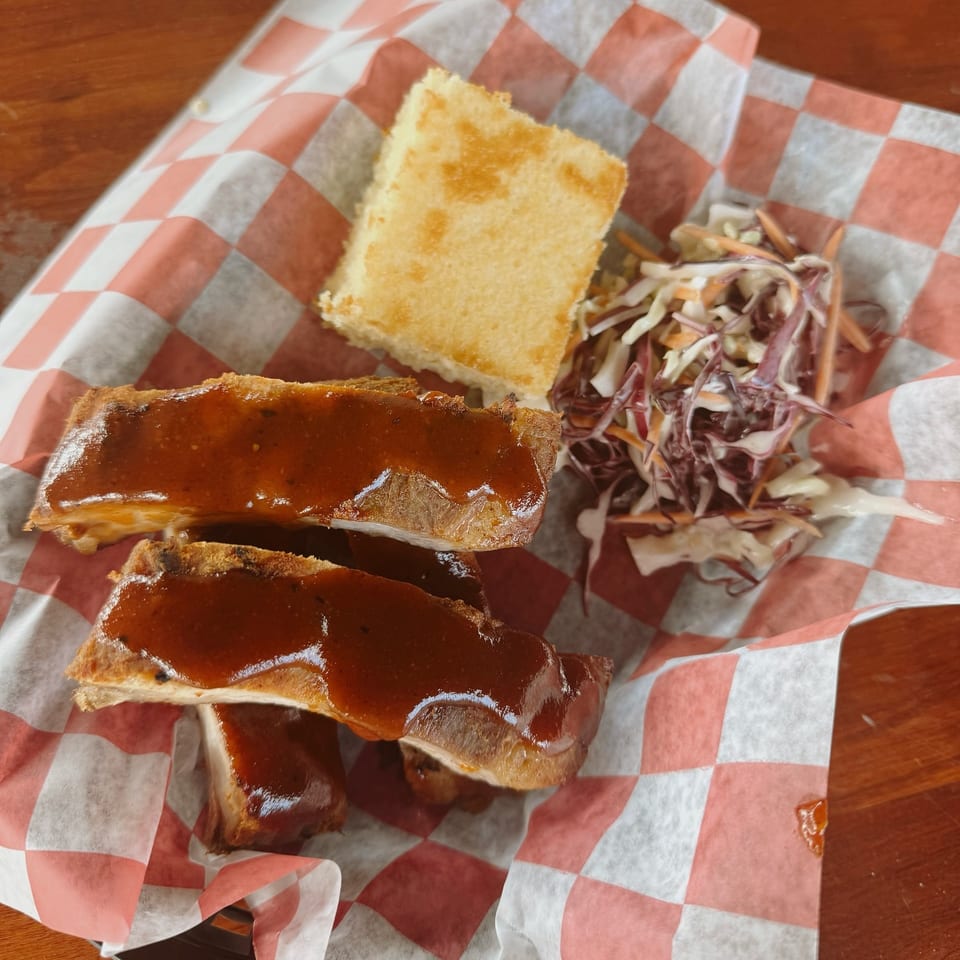 BBQ ribs with sauce, cornbread, and coleslaw on red and white checkered paper.