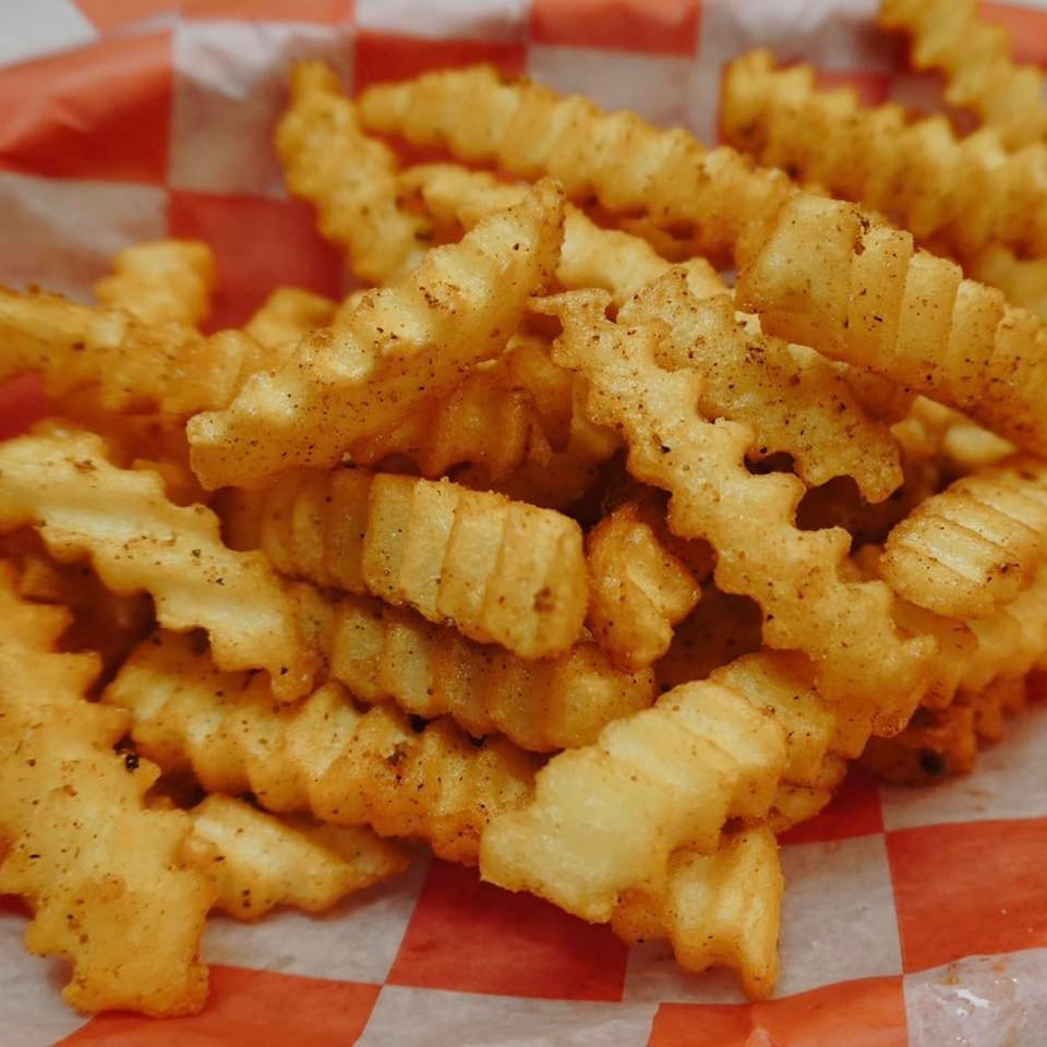 Close-up of crispy, seasoned crinkle-cut fries in a red and white checkered paper basket.